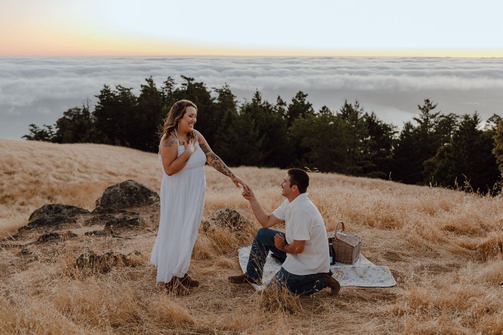 A romantic proposal takes place on a hilltop overlooking a sea of clouds at sunset.