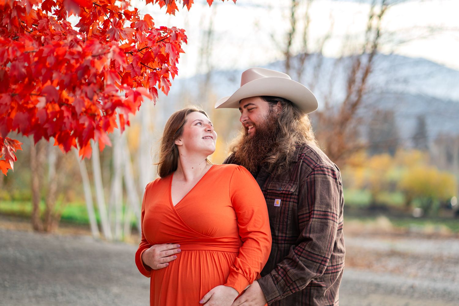 young couple enjoys a moment by a red tree while preparing for baby girl's arrival