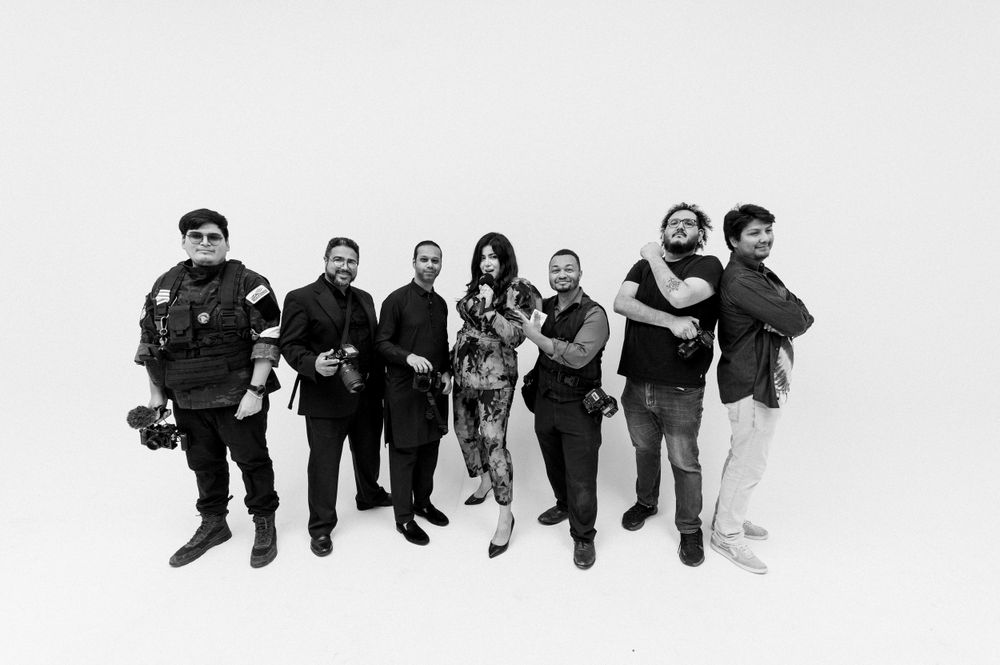 Black and white photo of a diverse group of eight people standing in a line against a white backdrop.