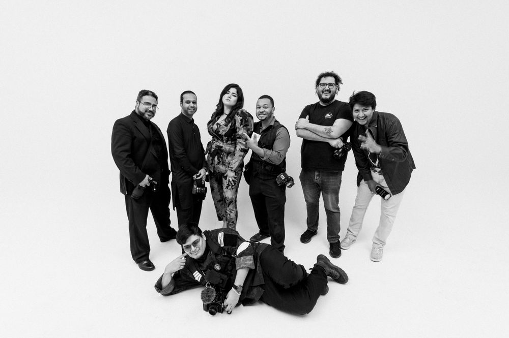 Black and white photo showing a diverse group of eight people arranged in casual poses against a white background.