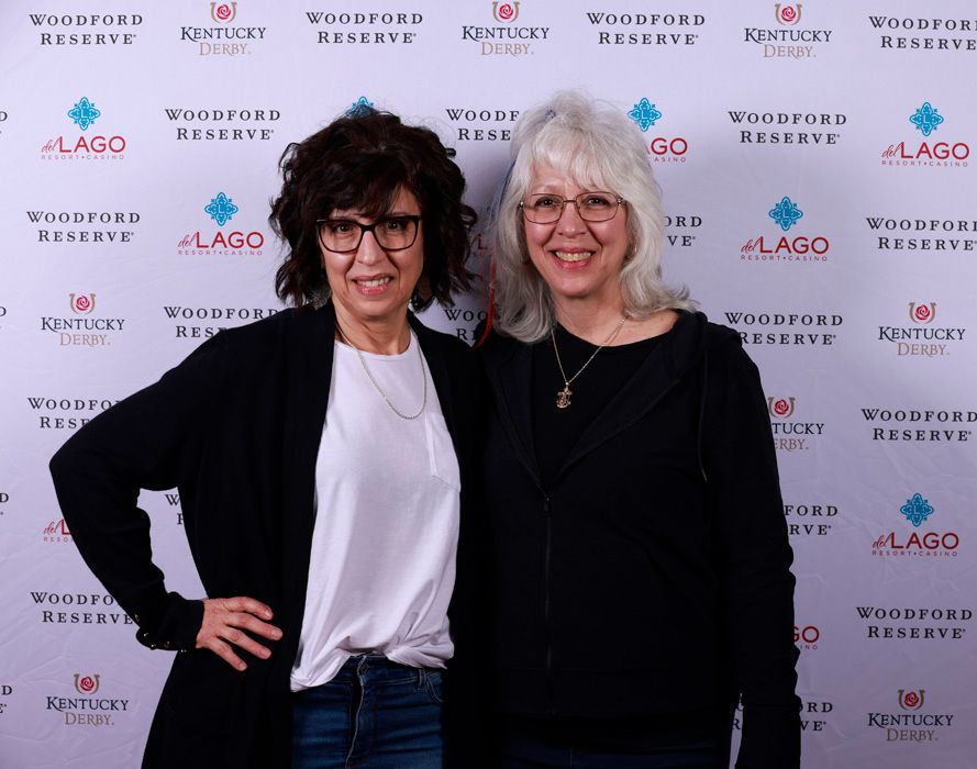 Two people posing in front of a branded step-and-repeat banner at a formal event.