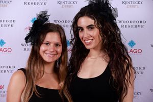 Two people in sleeveless tops smile while posing together at an event with Woodford Reserve branding in the background.
