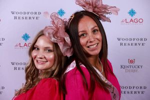 Two people wearing pink dresses and matching rose-colored fascinators pose together at a Woodford Reserve Kentucky Derby event.