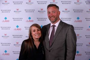 Guests in evening attire smile together at Woodford Reserve branded step-and-repeat wall.