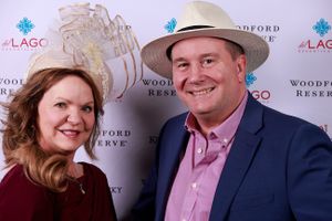 Two people in formal attire pose together at an event with Woodford Reserve branding on the backdrop wall.
