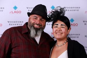 Two party guests pose together at a Woodford Reserve event with a branded step-and-repeat backdrop.