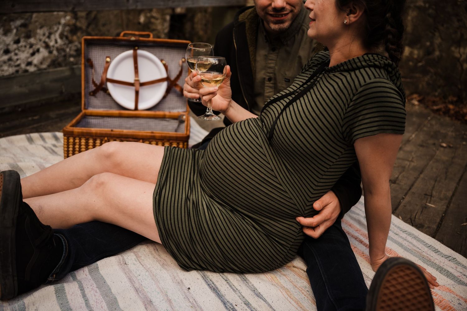 Expectant couple sharing drinks during picnic on wooden platform.