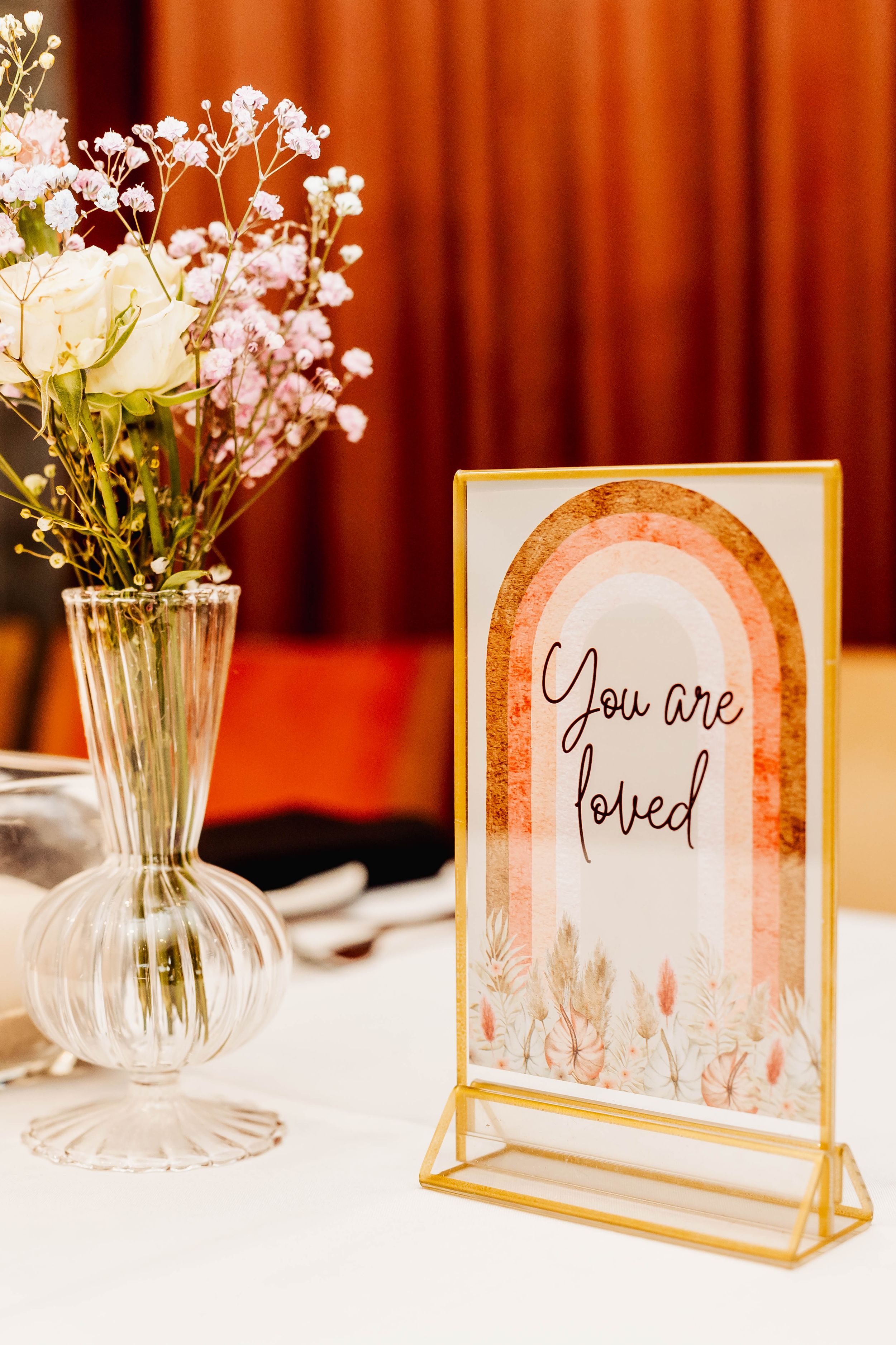 Elegant table setting with 'You are loved' sign in gold frame and delicate floral arrangement.