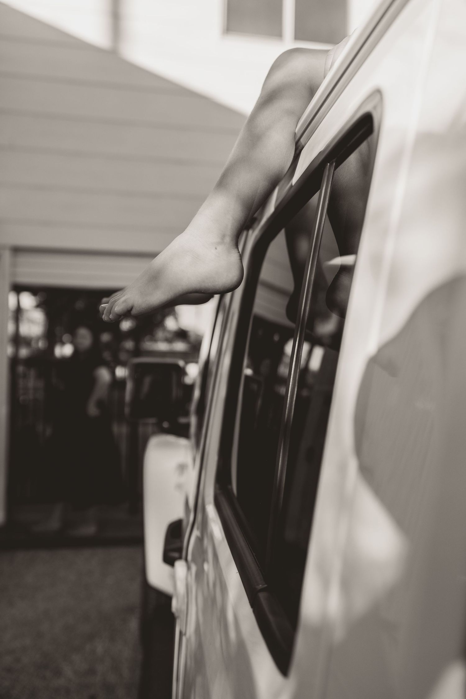 Bare feet hanging out of car window in black and white photo.