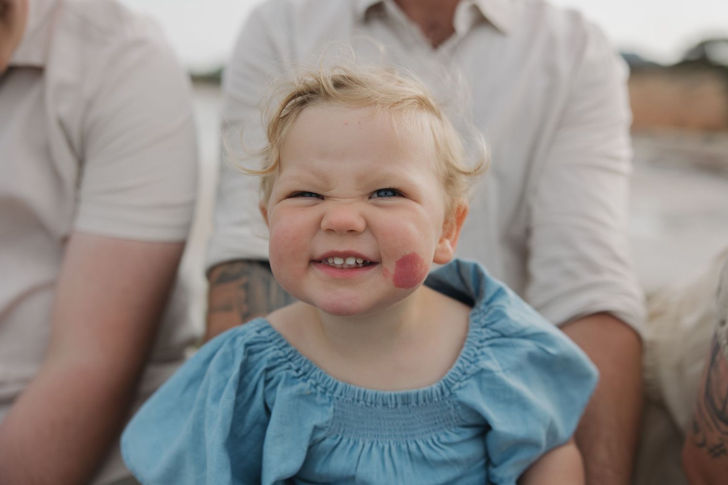Child wearing blue dress smiles brightly in outdoor portrait.