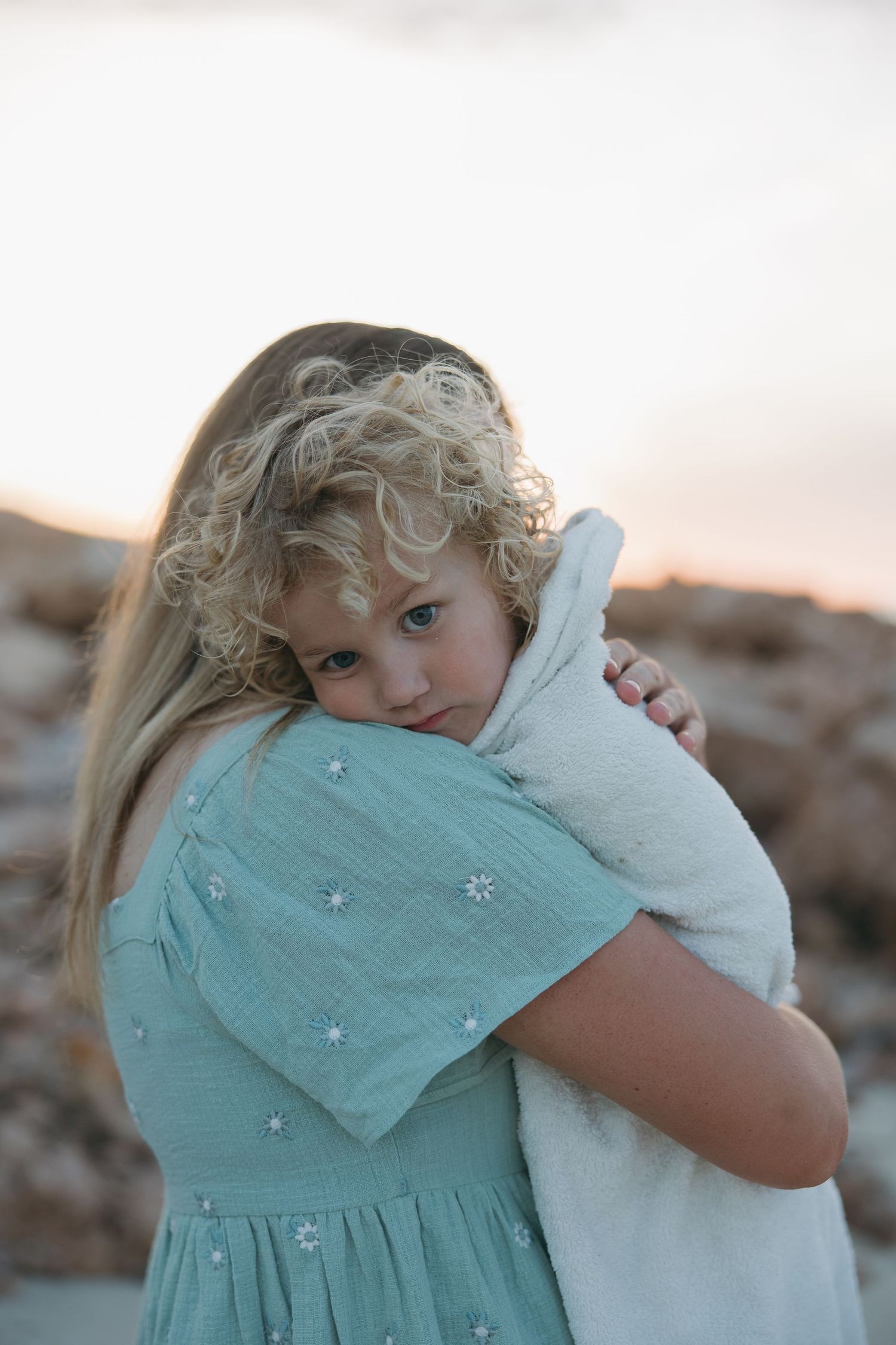 Child in turquoise dress hugging something close during sunset.