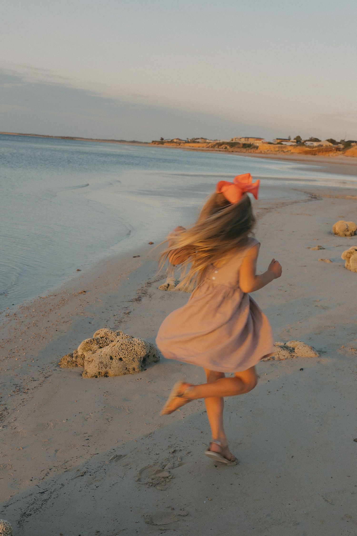 Figure in a flowing dress dances joyfully along the beach at sunset.