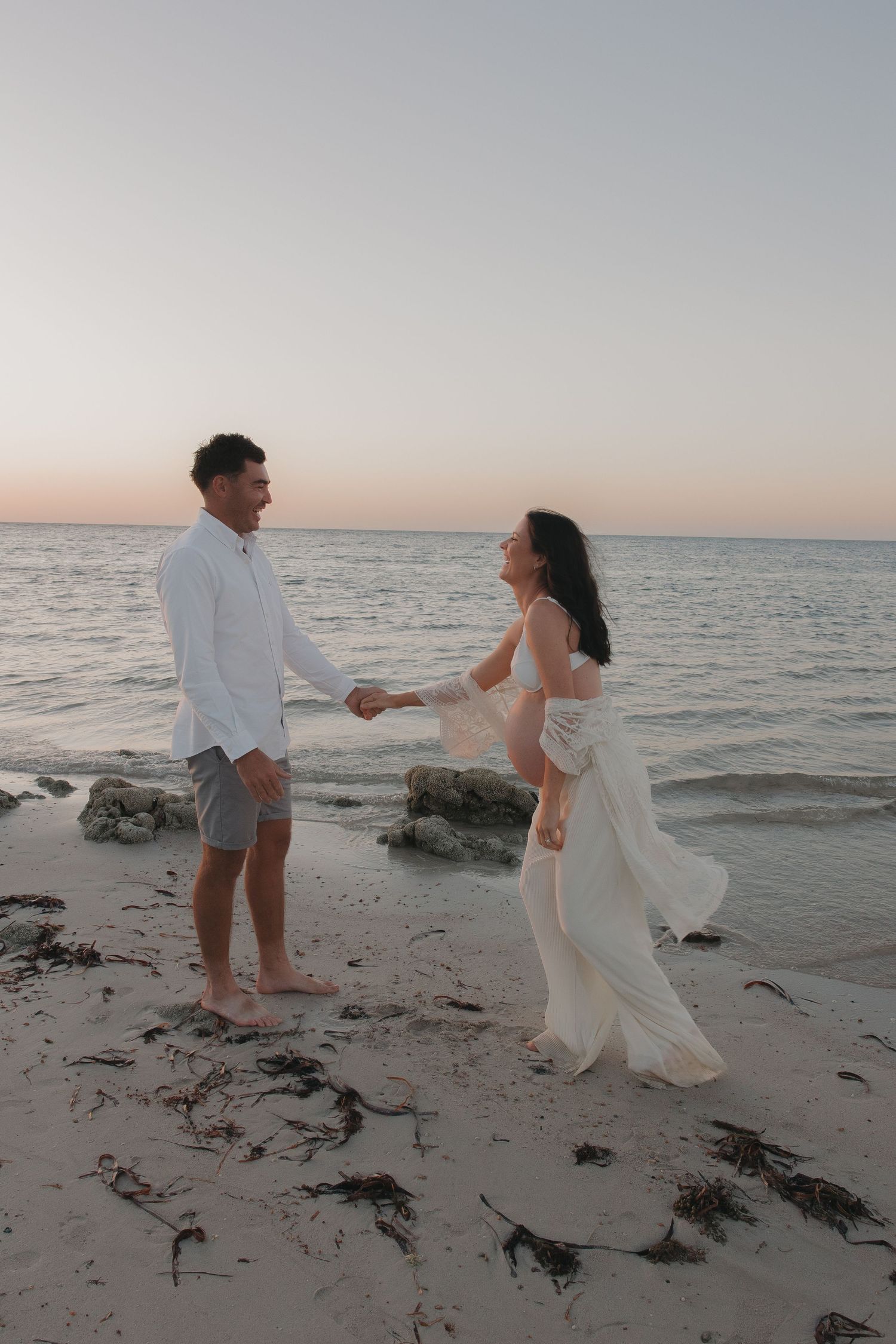 Couple holding hands and dancing playfully on beach at sunset.