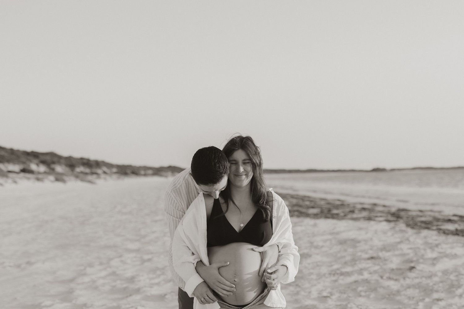 An intimate black and white beach portrait of an expecting couple sharing a tender moment.