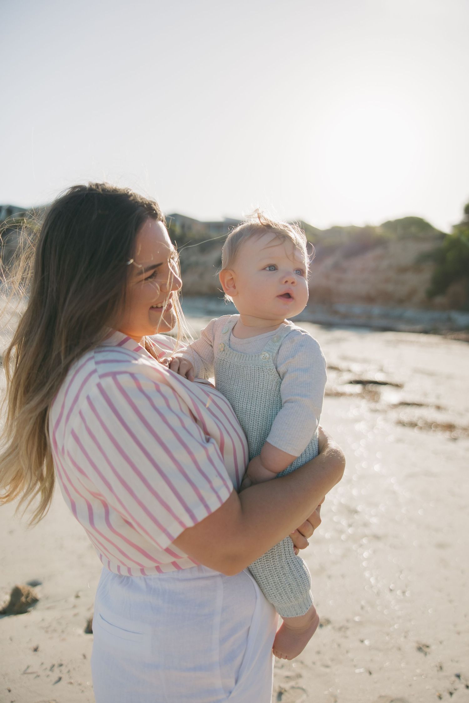 Mother and baby sharing a joyful moment on the beach in golden sunlight.
