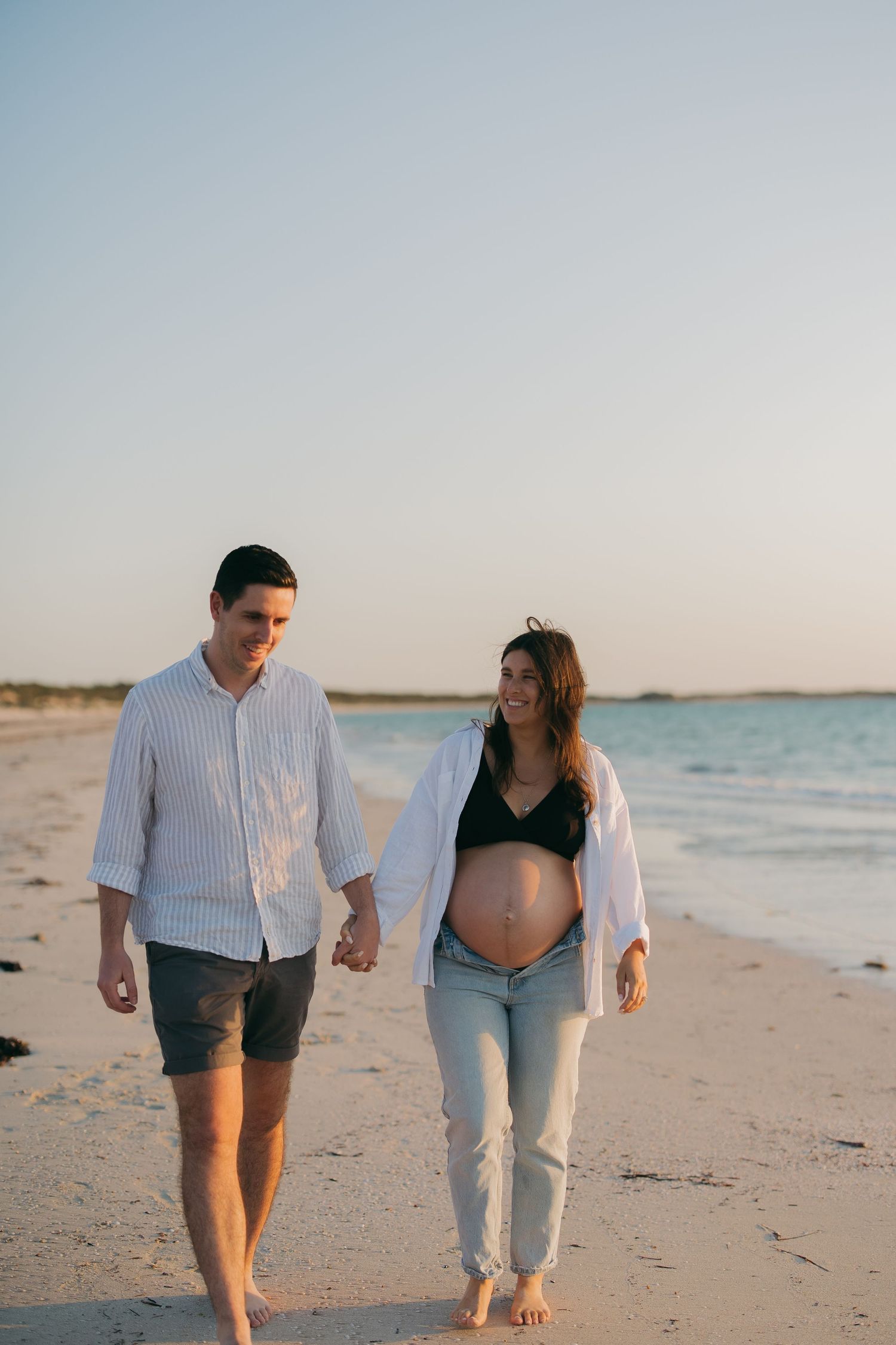 A couple takes a romantic beach walk together at sunset, with waves gently lapping the shore.