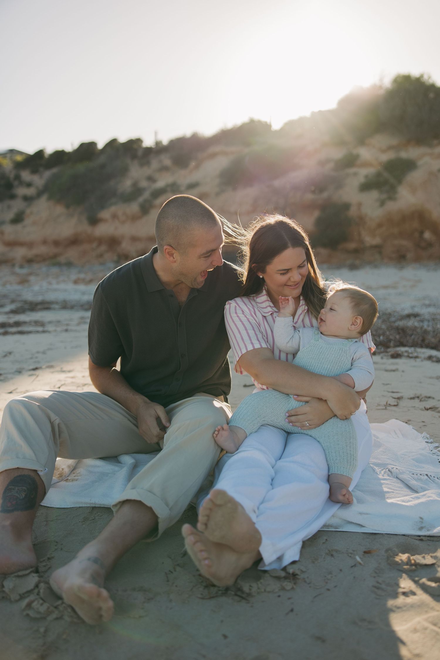 Family enjoying a tender moment together on a sandy beach at sunset.