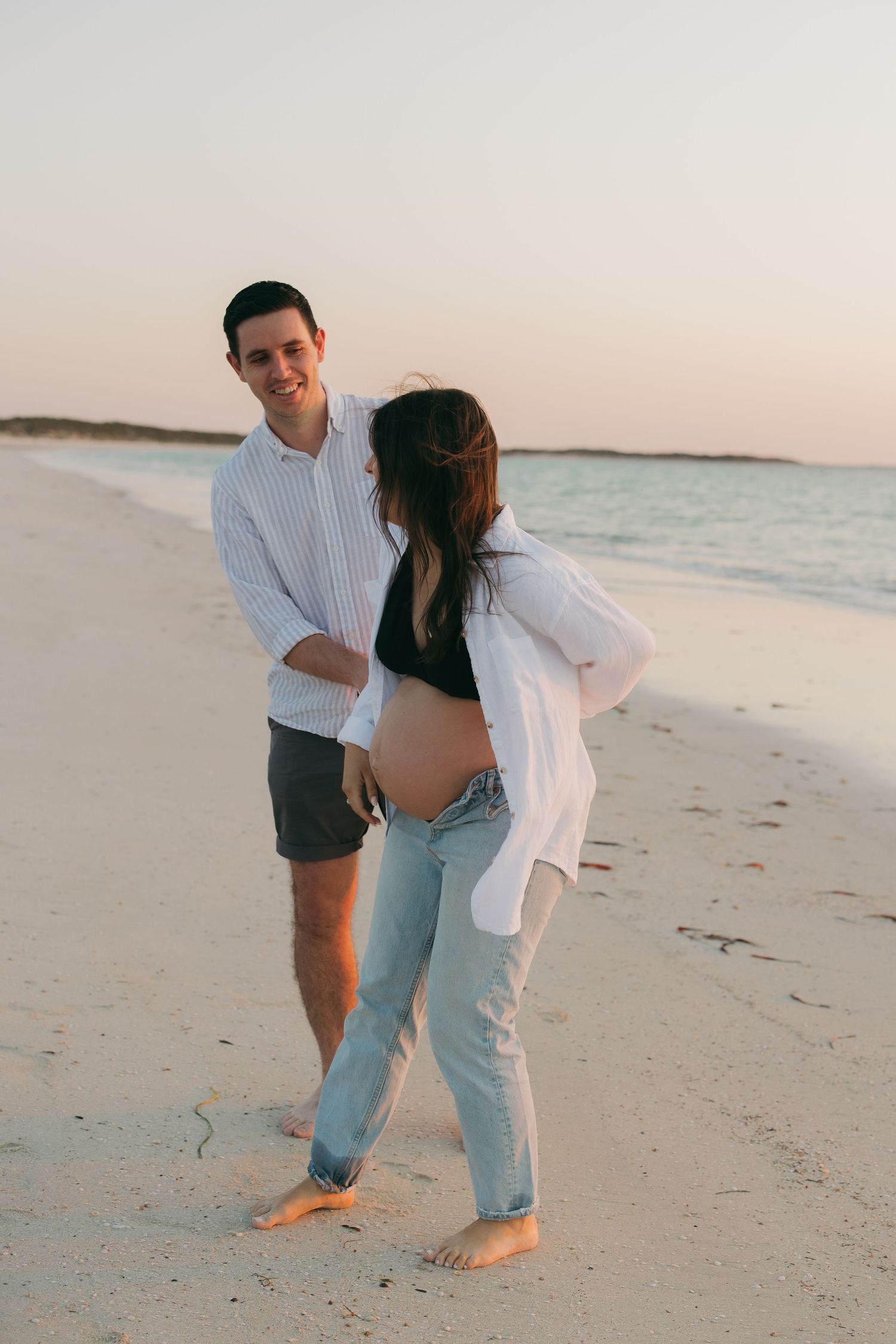 A couple enjoys a playful moment together on a peaceful beach during sunset.