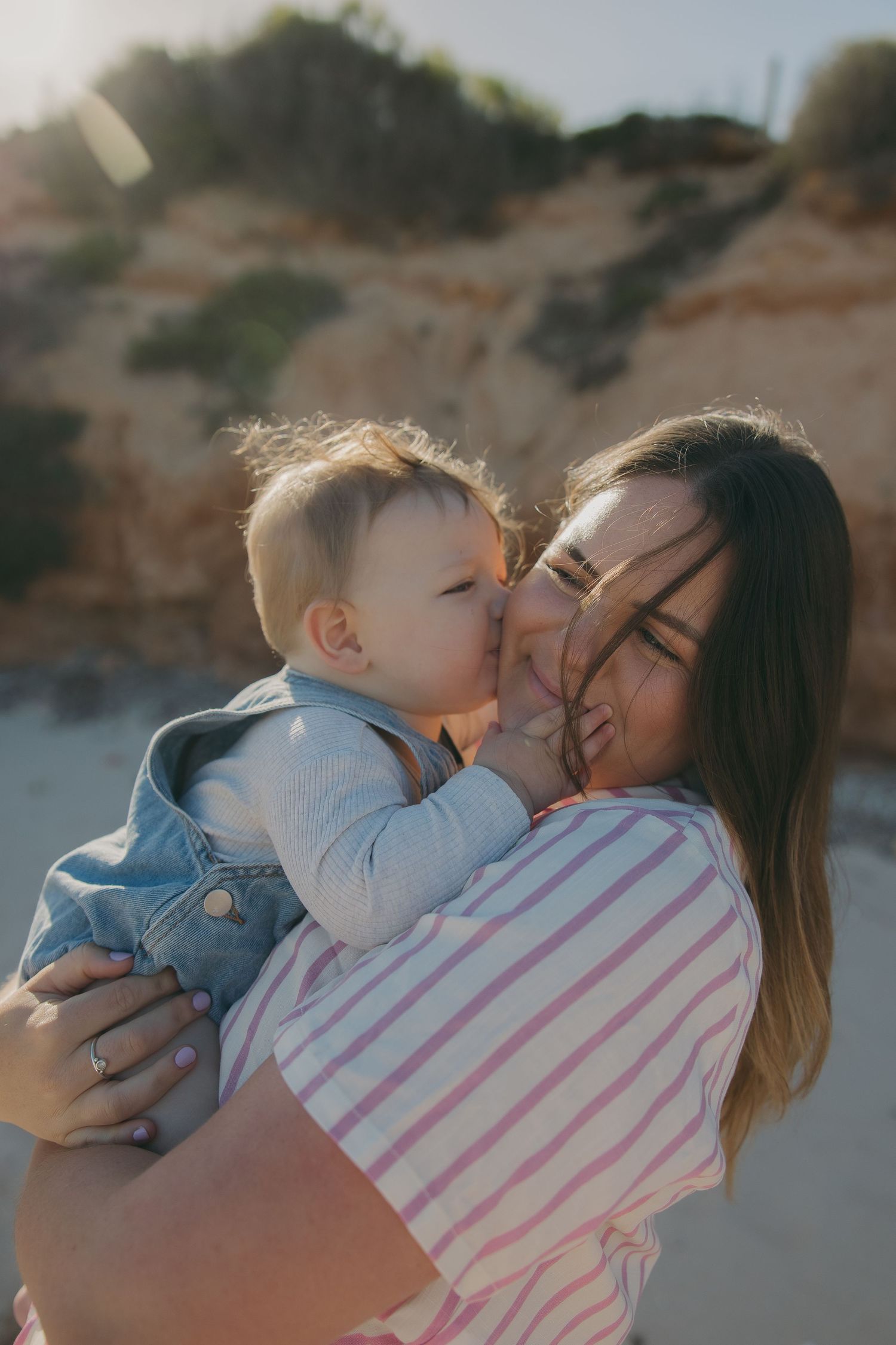 Sweet embrace between parent and baby against coastal cliffs at sunset.