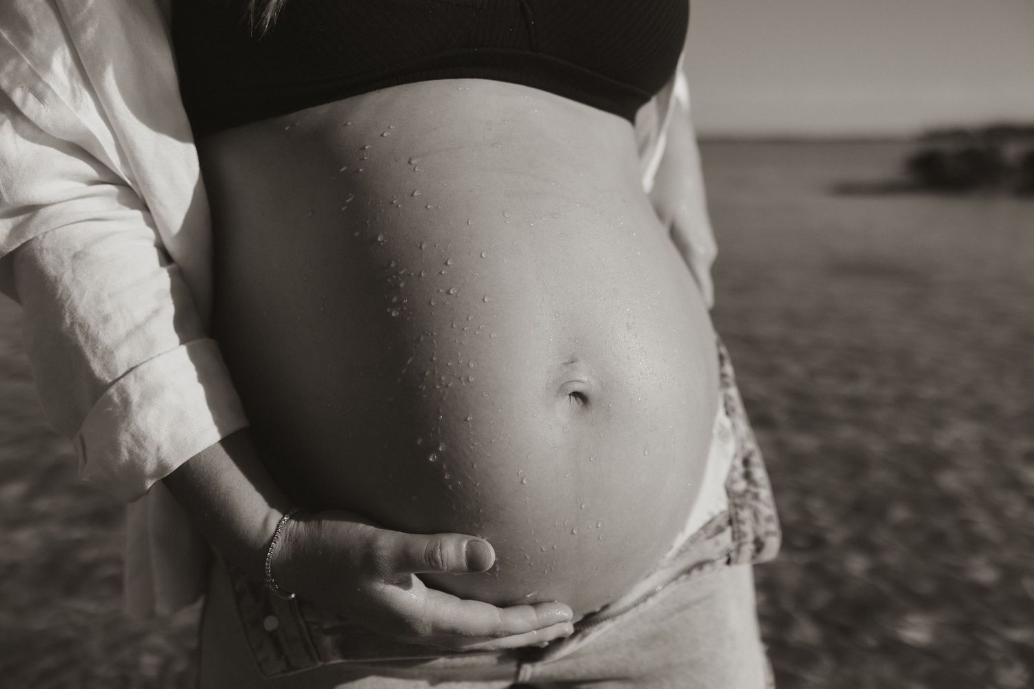 Close up of pregnant belly being cradled by hands in black and white.