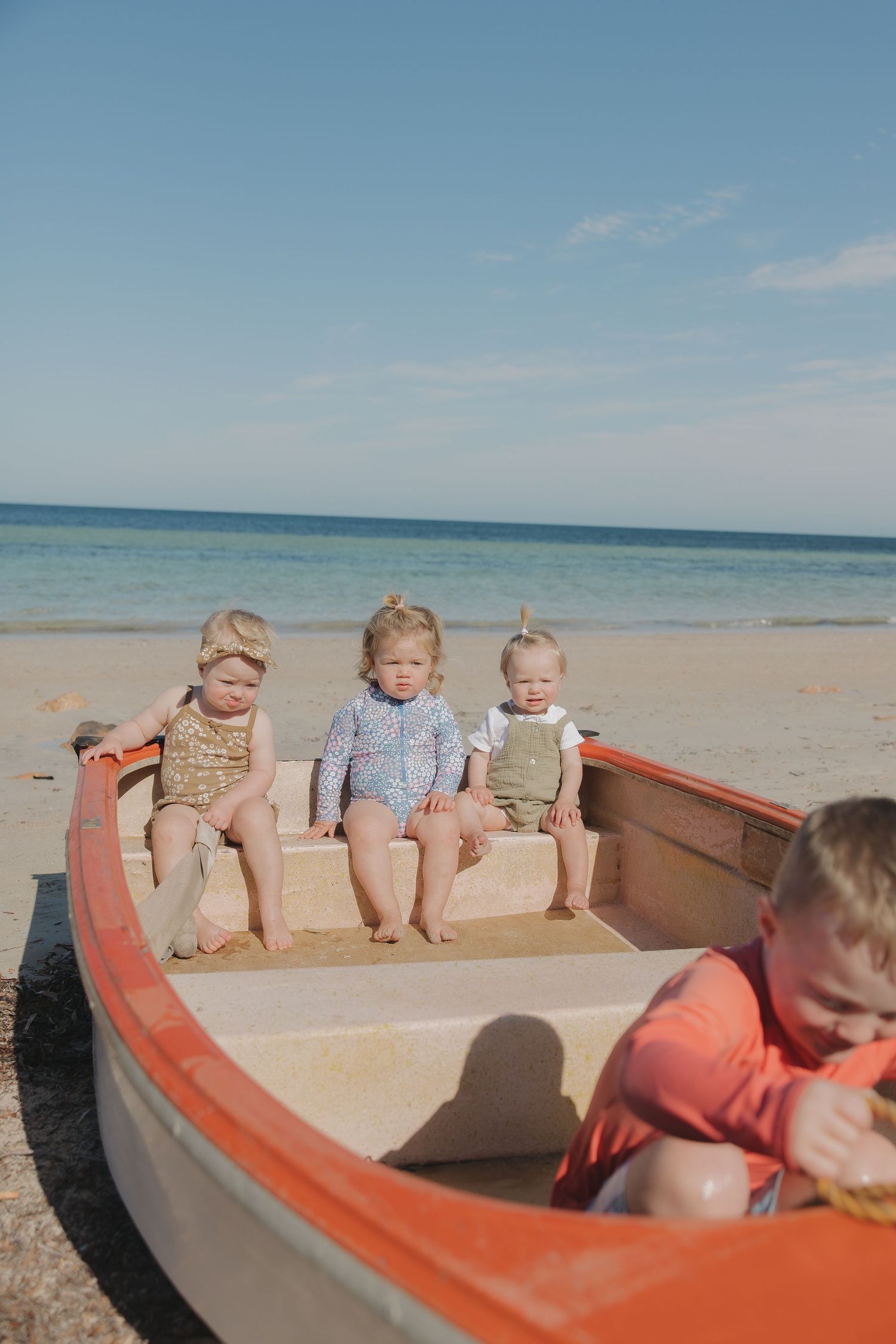 Children sitting in red and white boat at the beach on sunny day.