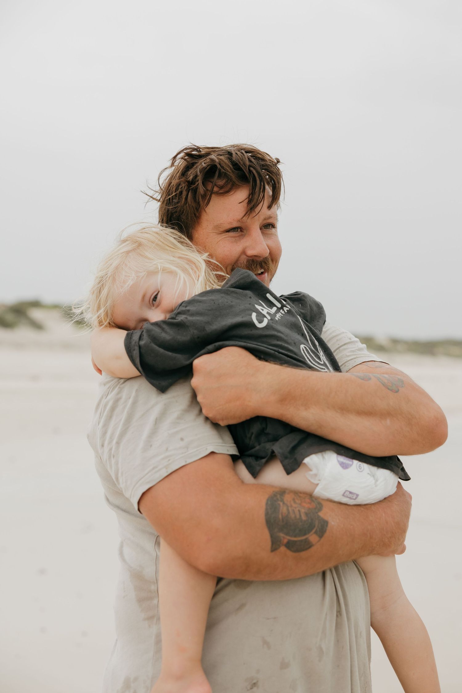 A joyful moment shared between parent and child on a cloudy beach day.