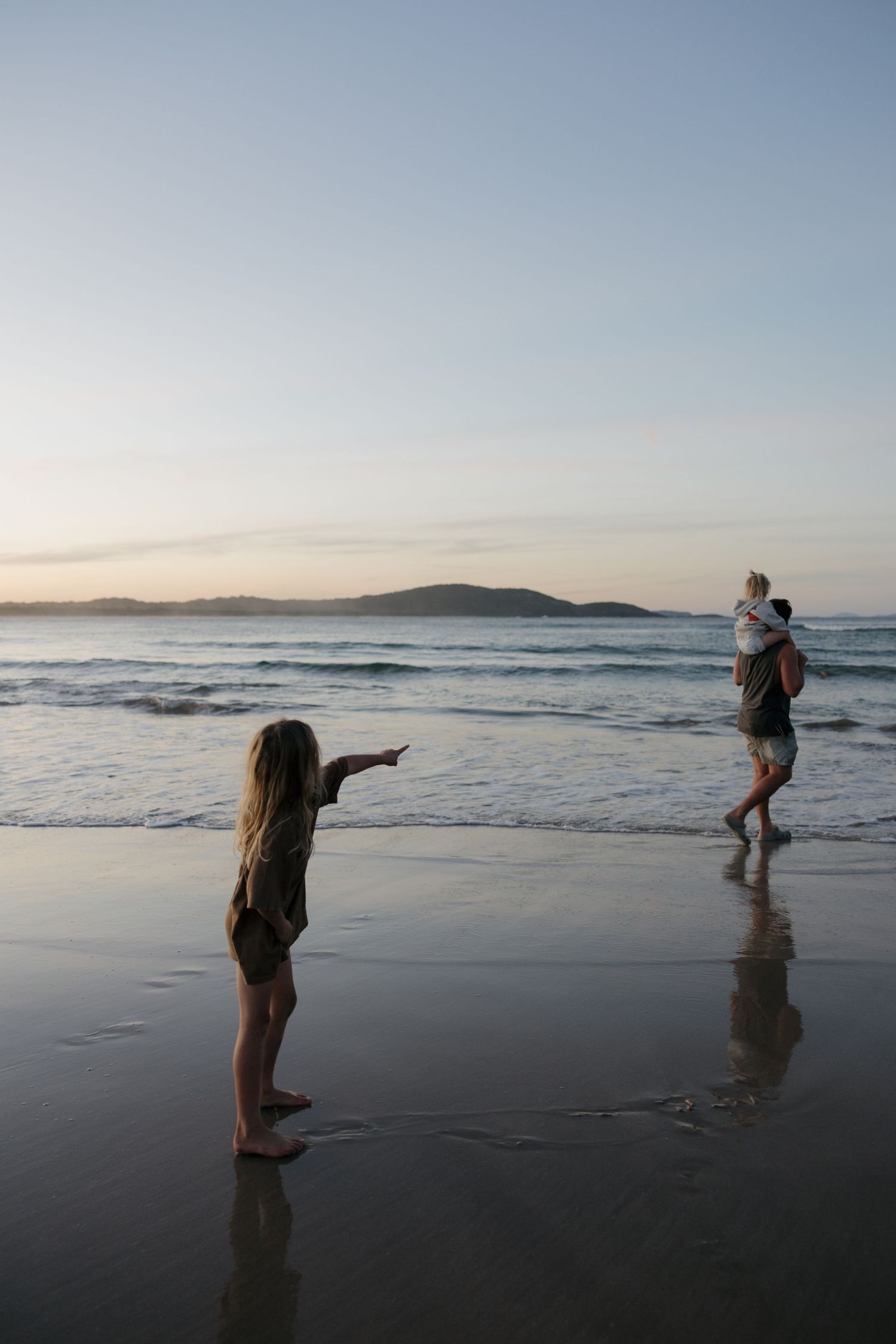 Silhouettes of people playing on the beach at dusk with mountains visible in the distance.