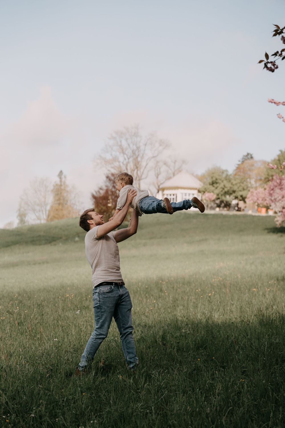 Person in jeans and brown sweater stands in a green grassy field enjoying autumn weather outdoors on a cloudy day.