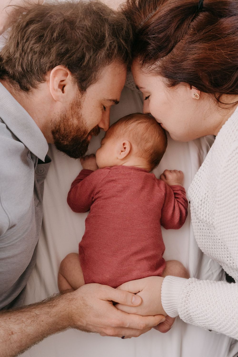 Intimate family portrait with parents and newborn baby in rustic colors against white background.