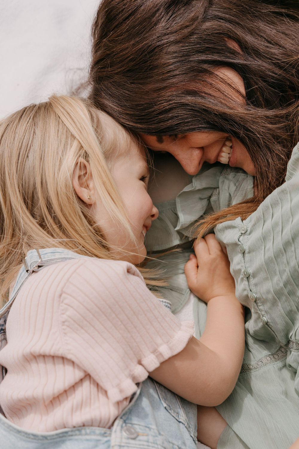 Tender moment shows close-up of loving parent and child in soft blush pink and sage green tones snuggling together.