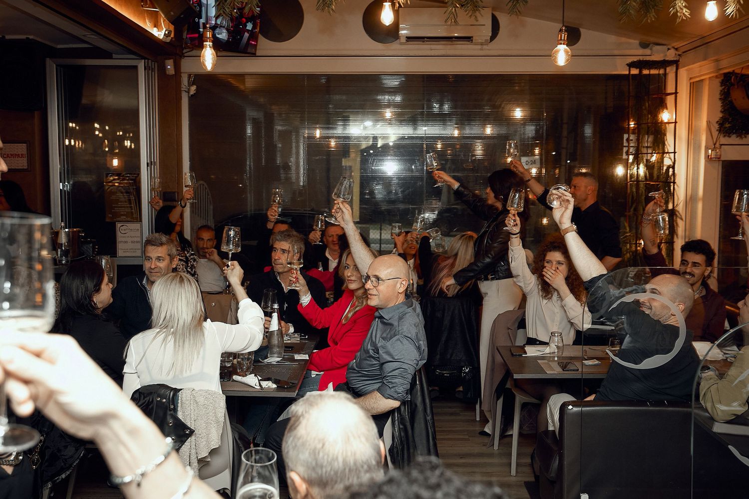Crowd of people raising their glasses in celebration at a dimly lit restaurant.
