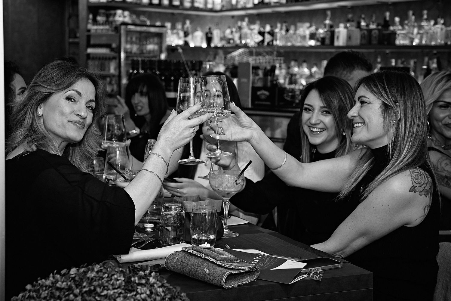 Friends toasting with wine glasses at a bar in black and white.