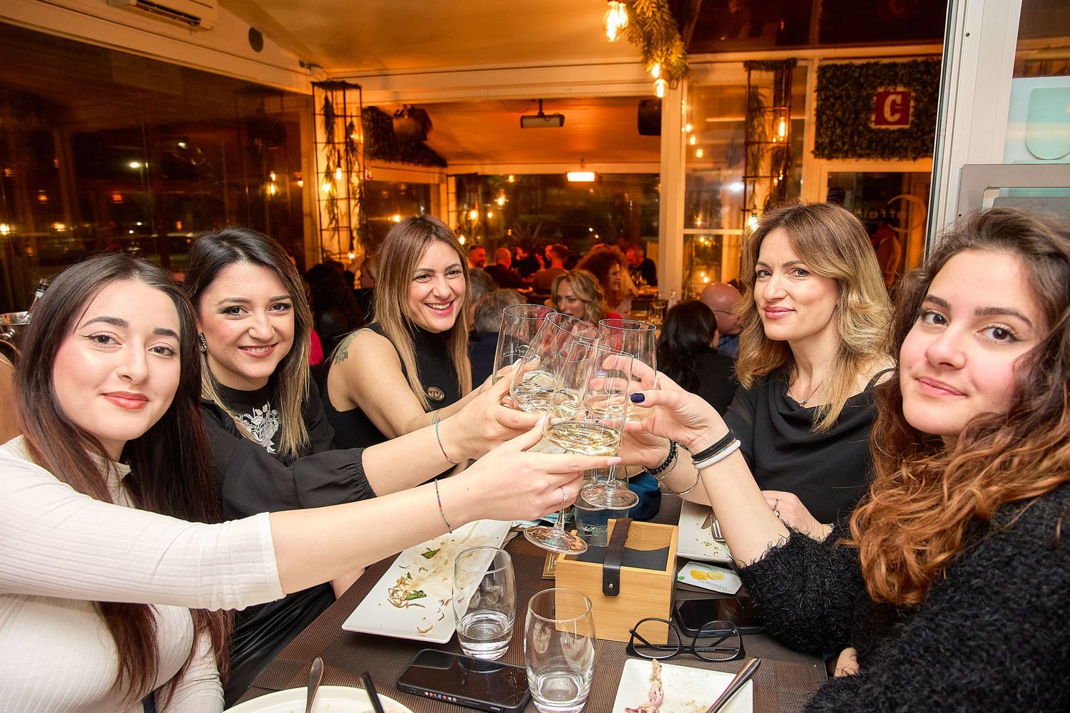 Friends celebrating with raised glasses around restaurant table.