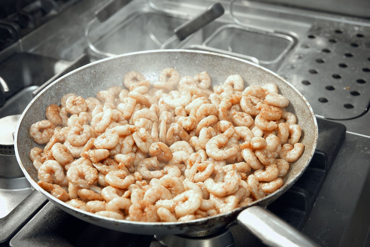 Raw shrimp cooking in stainless steel pan on professional kitchen stove.