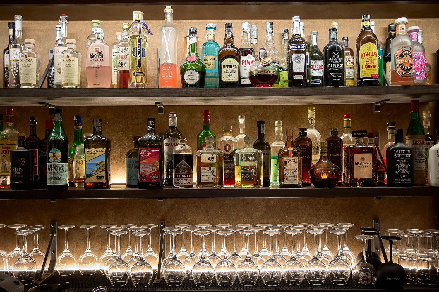 Well-stocked bar shelves display various liquor bottles with cocktail glasses arranged below.