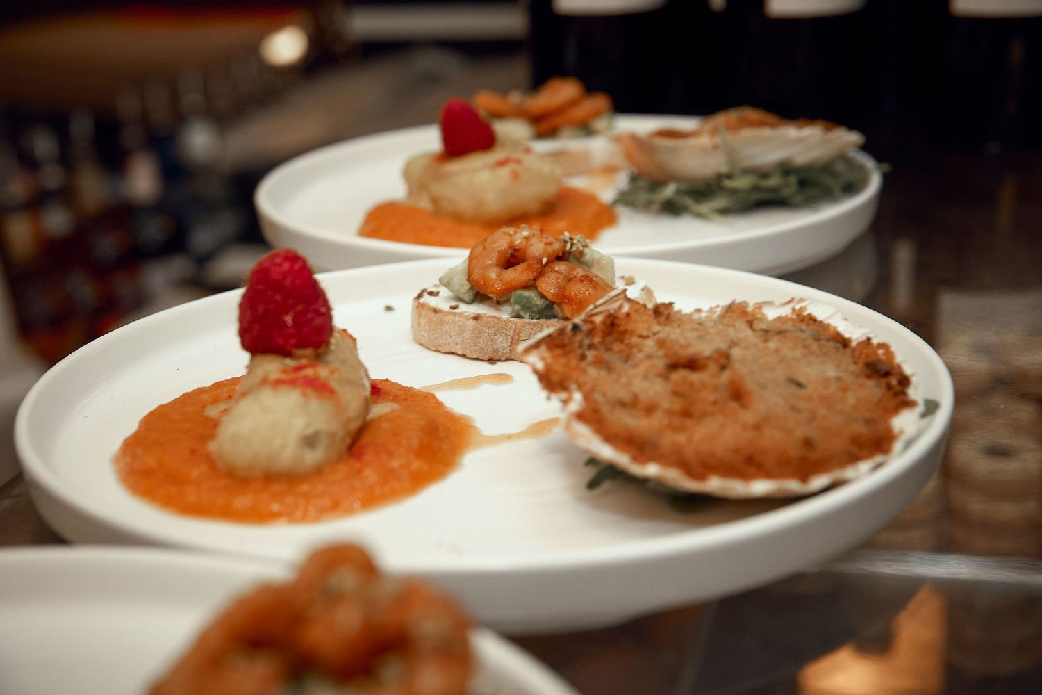 Elegant seafood appetizers with raspberry garnishes served on white plates.