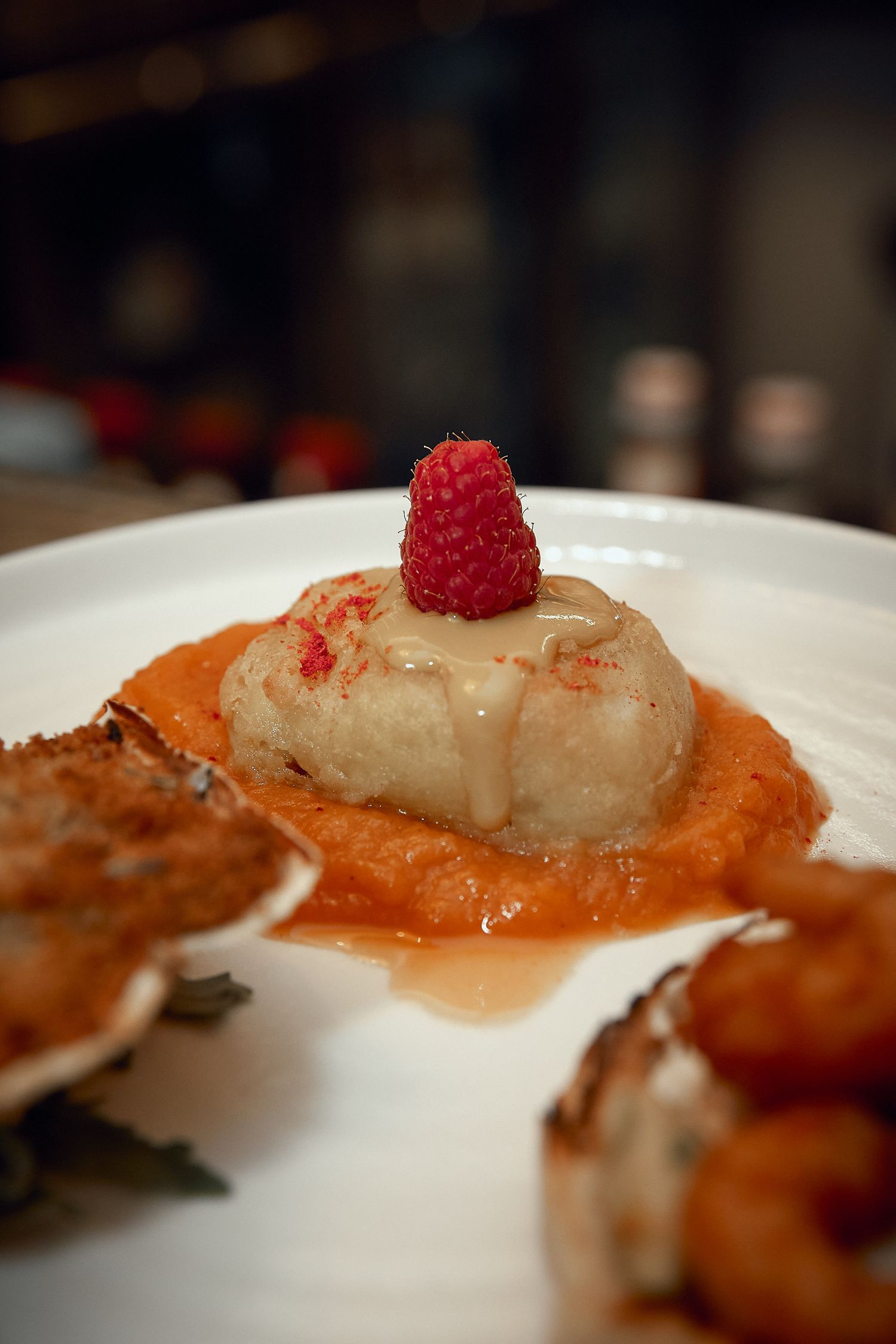 Gourmet seafood dish with raspberry garnish in orange sauce on white plate.