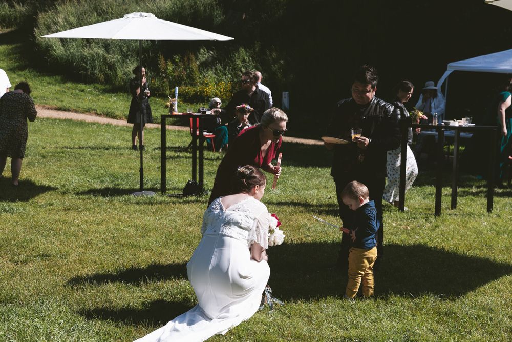 Children play games on the lawn at an outdoor wedding reception with white tents.