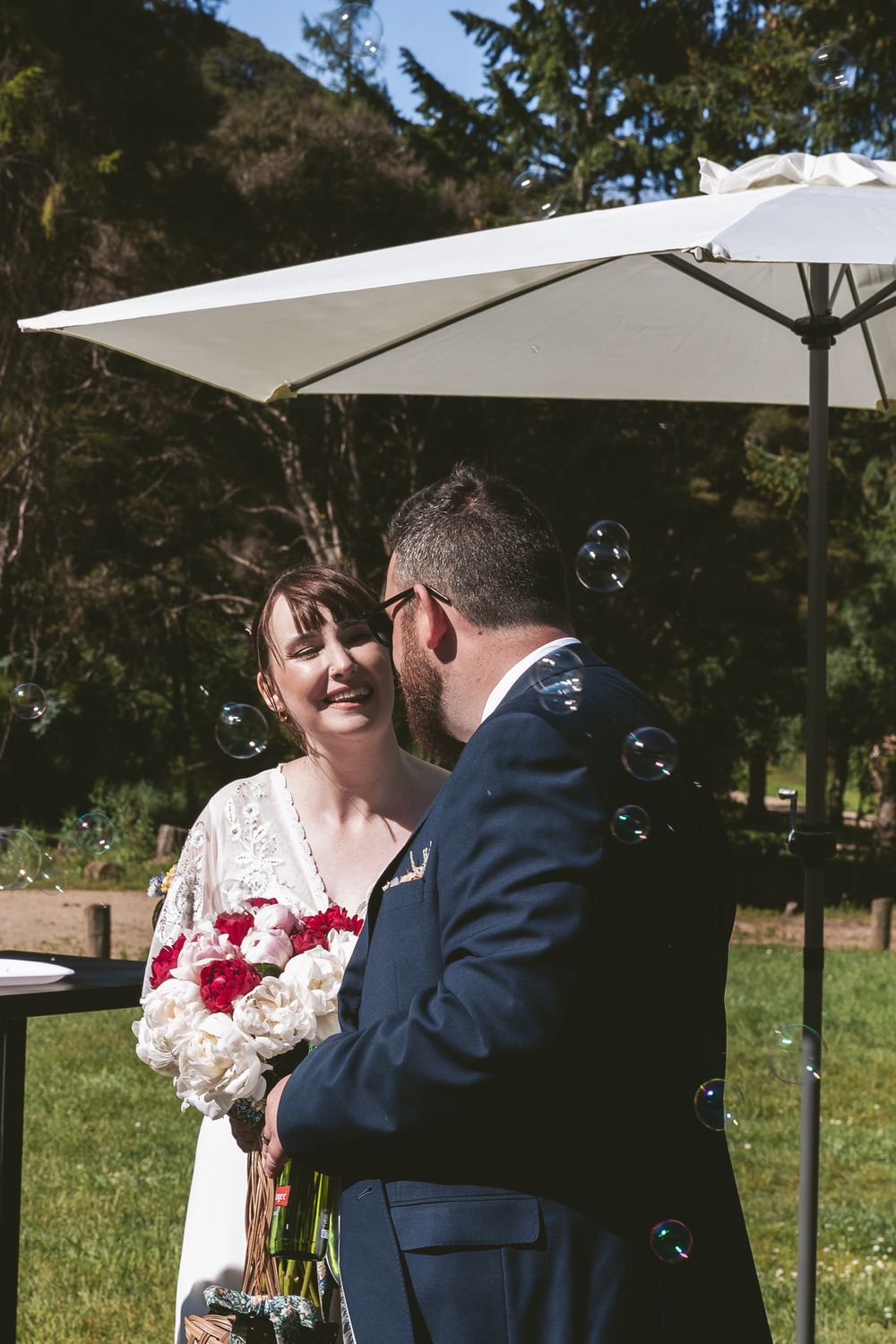 A tender moment between newlyweds under a white umbrella at their outdoor wedding.