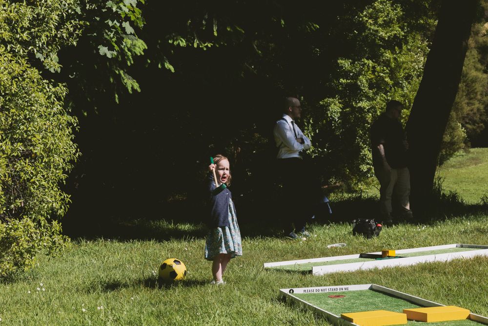 Child playing on a lawn with outdoor games set up at a wedding reception.