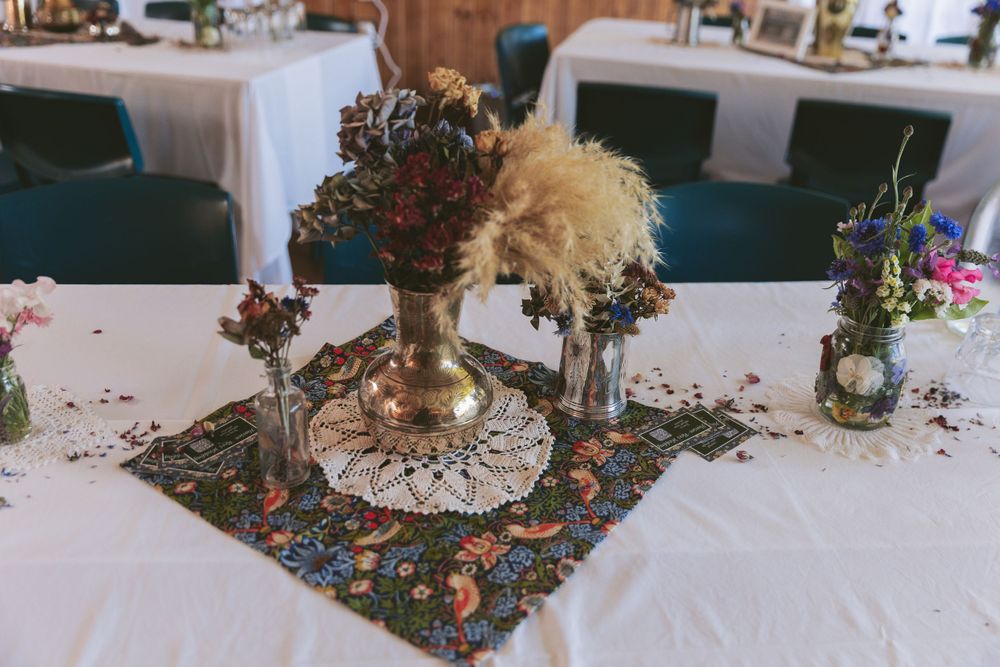Rustic wedding centerpiece featuring dried flowers and lace doilies on white tablecloth.