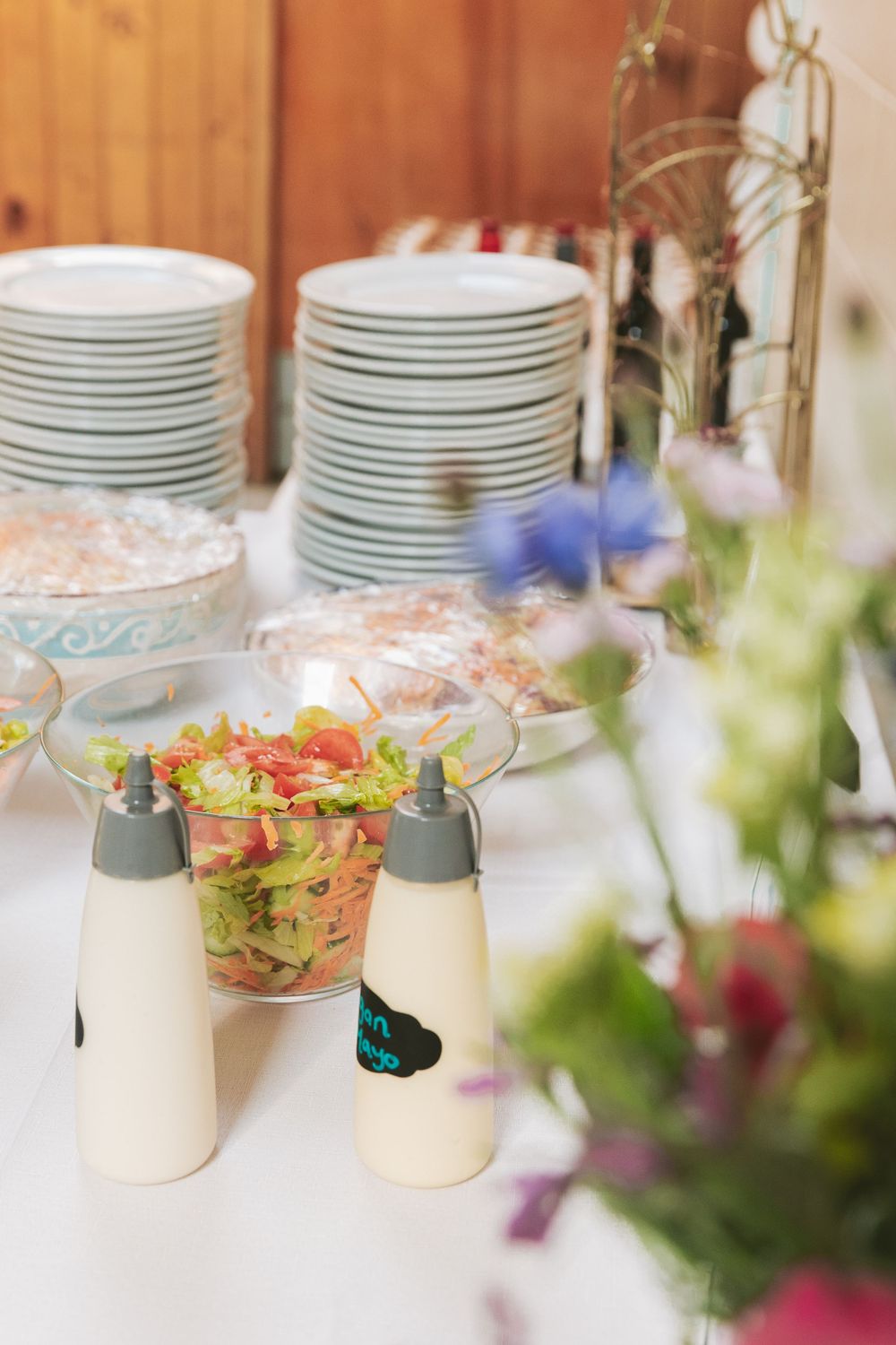 Table setting with stacked plates and colorful flower arrangements near white condiment bottles.