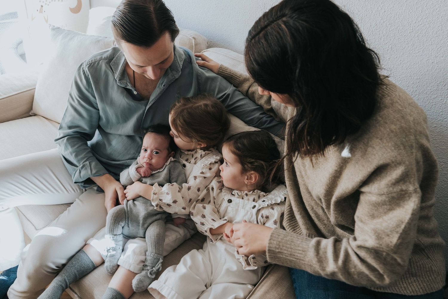 familia con tres hijos sentados en el sofá durante una sesión de fotos familiar natural en casa en Madrid