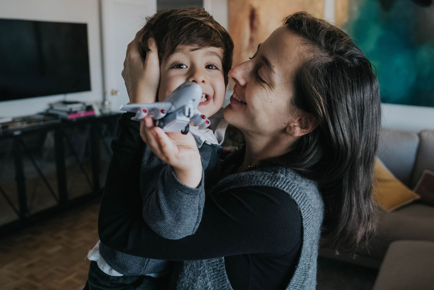 madre abrazando a su hijo con un avión de juguete durante una sesión de fotos familiar en casa en Madrid