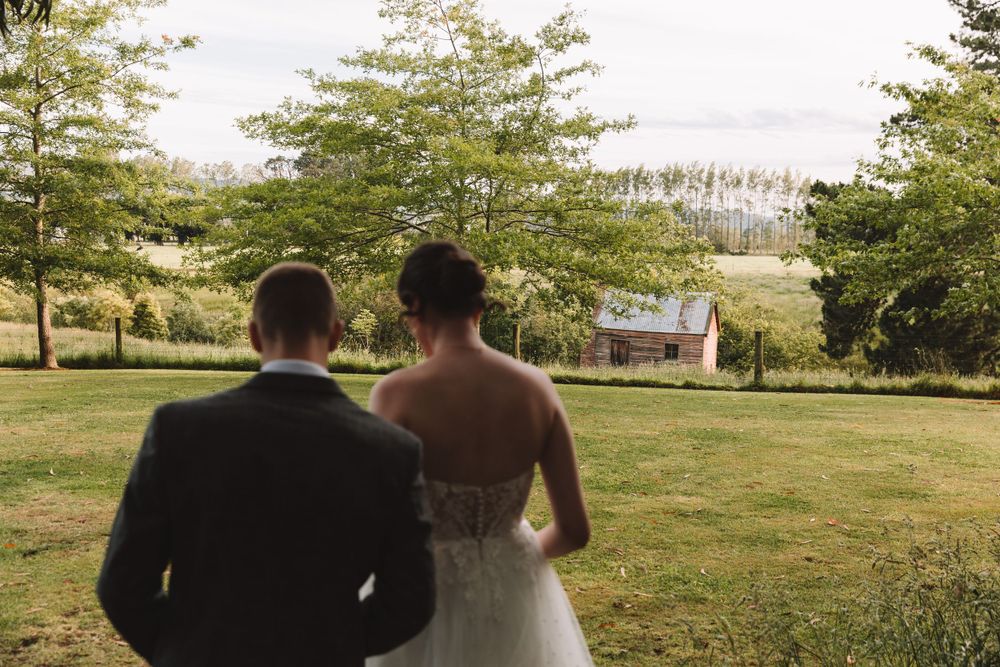 Back view of newlyweds looking towards a distant house in a rural setting.
