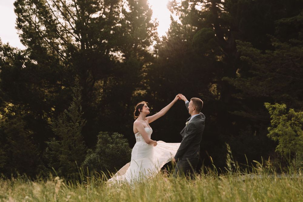 Wedding couple dancing joyfully in a meadow during golden hour.