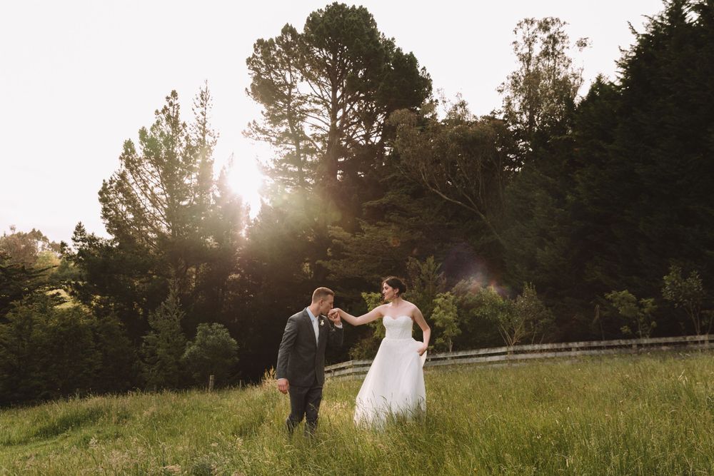 Newlyweds dance together in a sunlit meadow surrounded by evergreen trees.