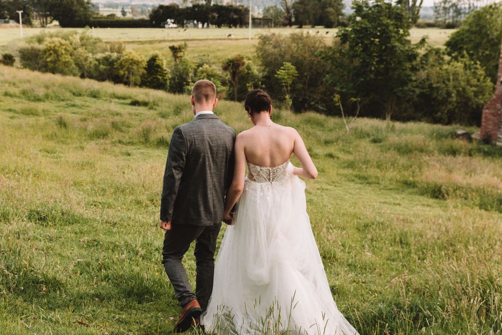 A couple walking hand in hand through tall grass on their wedding day.