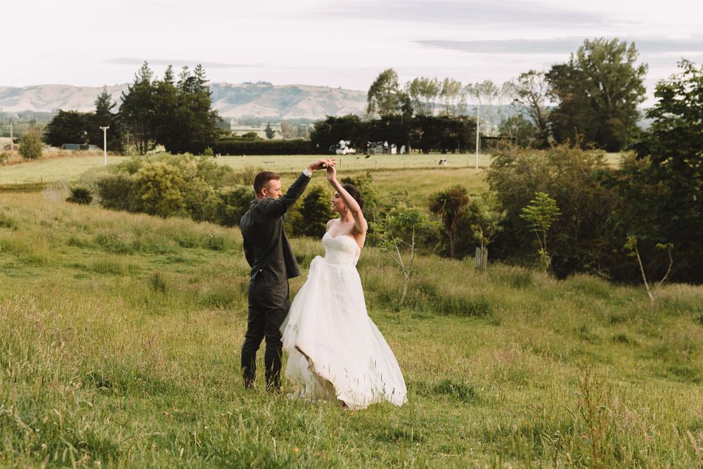 A joyful couple dancing in a hilltop meadow with the bride's dress flowing in the wind.