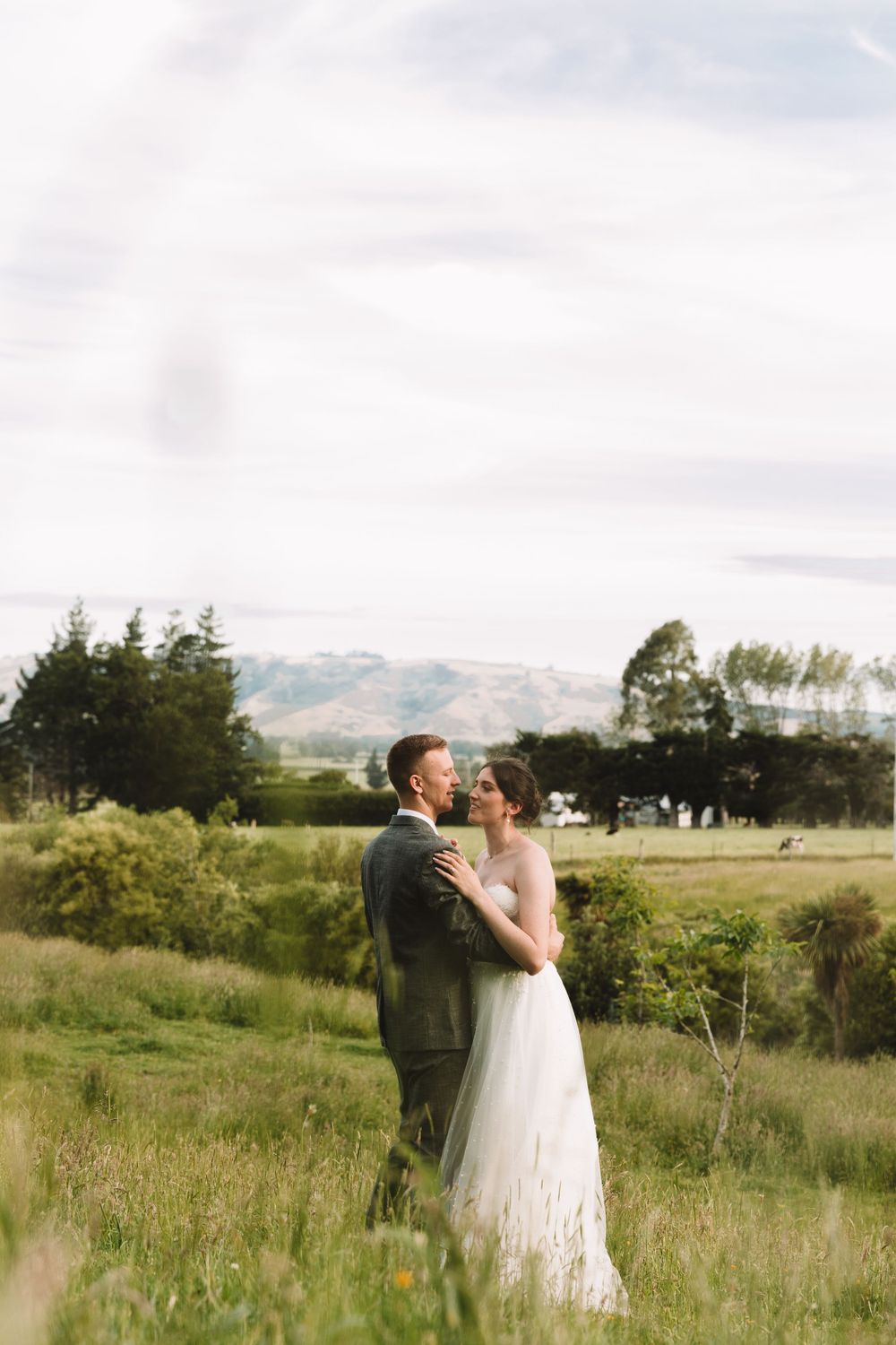 A romantic wedding portrait in a meadow with mountains visible in the distance.